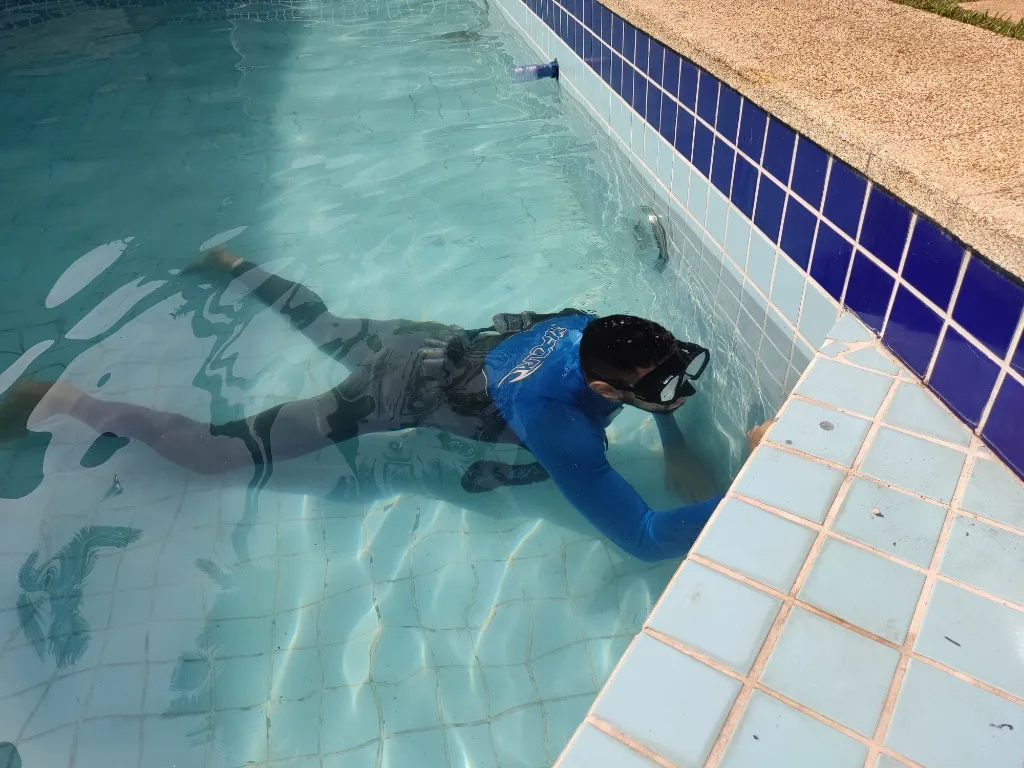 Técnico de caça vazamento realizando inspeção visual subaquática e detecção eletrônica em piscina